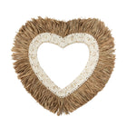 Heart-shaped decorative item with beige fringe and white floral center on a white background
