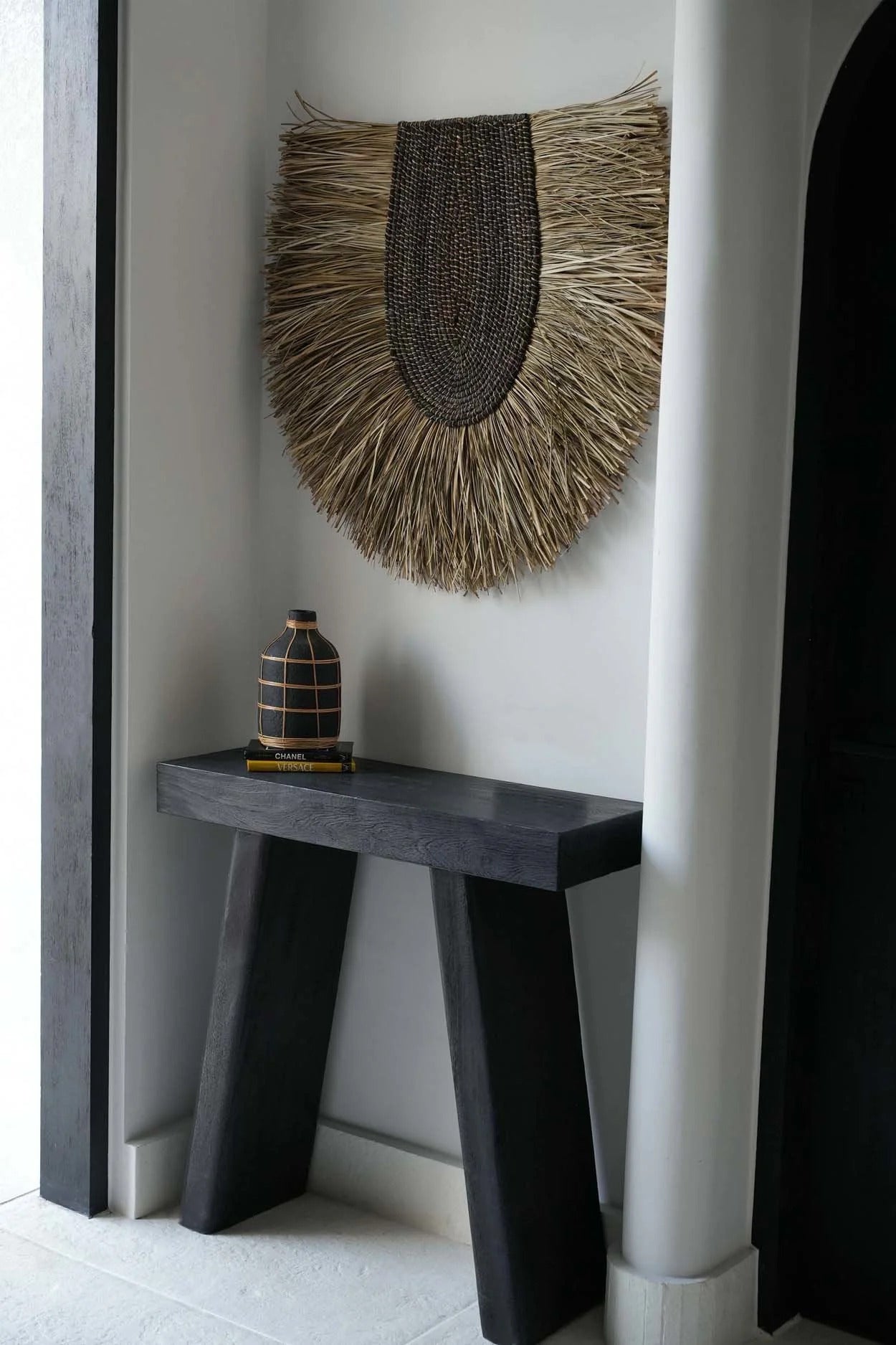 Decorative wall art with fringes on a white wall above a dark wooden console table.