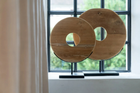 Teak Wood circular sculptures on a stand in front of a window with a view of greenery. close up.